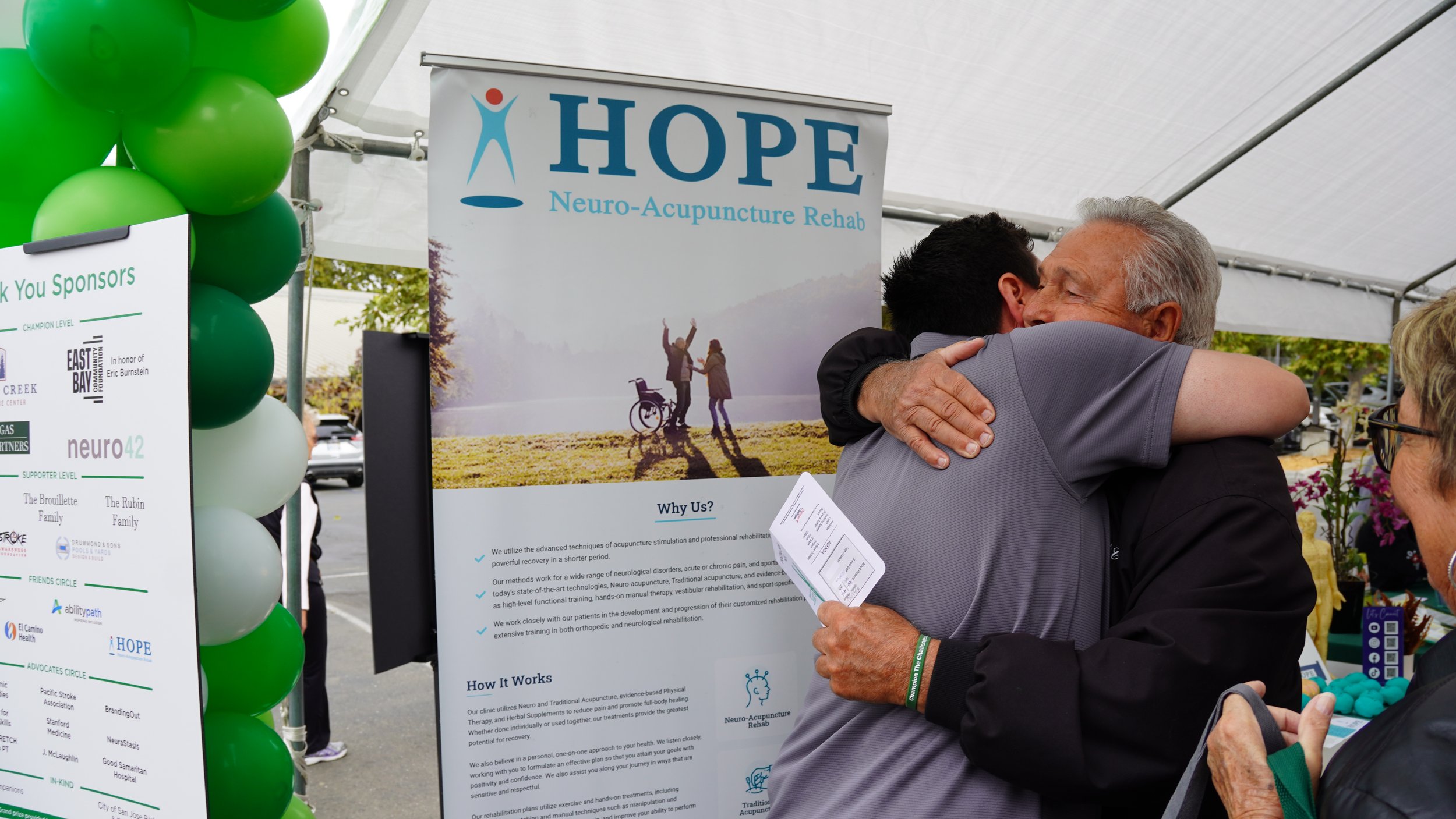 Attendee and staff member hugging at community stroke awareness event near HOPE banner