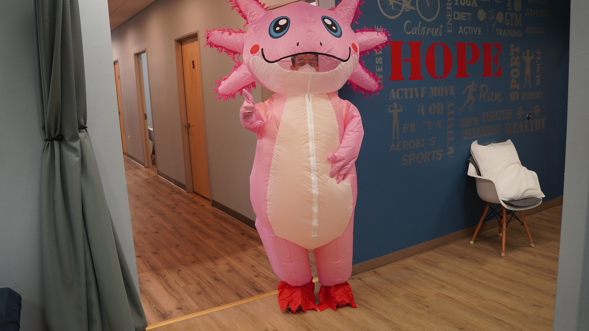 Staff member in inflatable pink axolotl costume posing in HOPE Clinic hallway