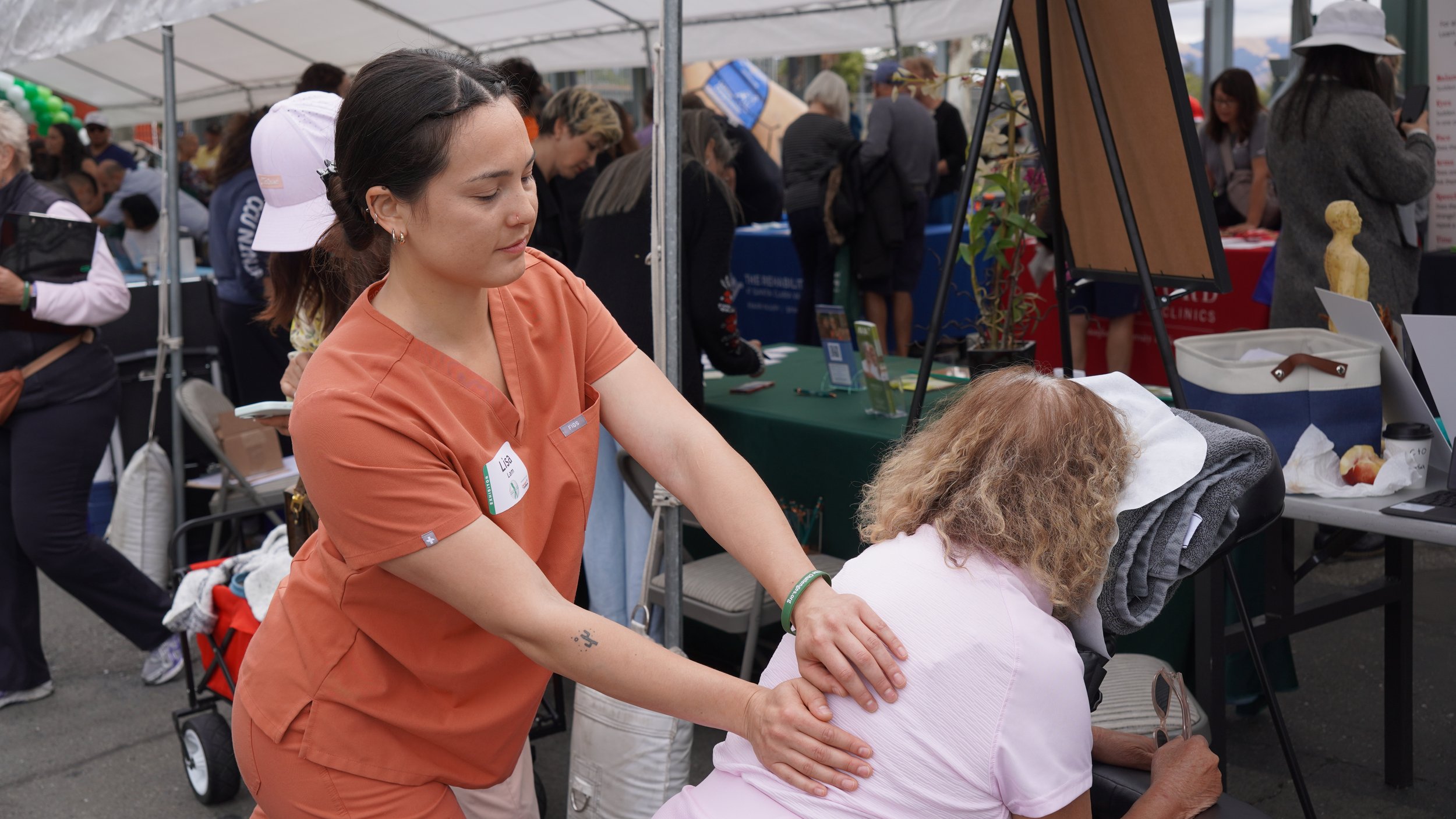 HOPE massage therapist providing shoulder massage to seated attendee at outdoor event