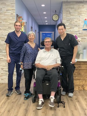 Therapy team and patient with wheelchair posing in clinic hallway