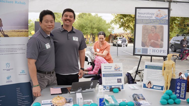 Dr. Lu and therapist standing at HOPE Clinic booth with neurology massage display