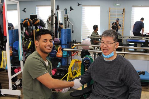 Physical therapy aide assisting smiling patient with hand exercises in rehab gym