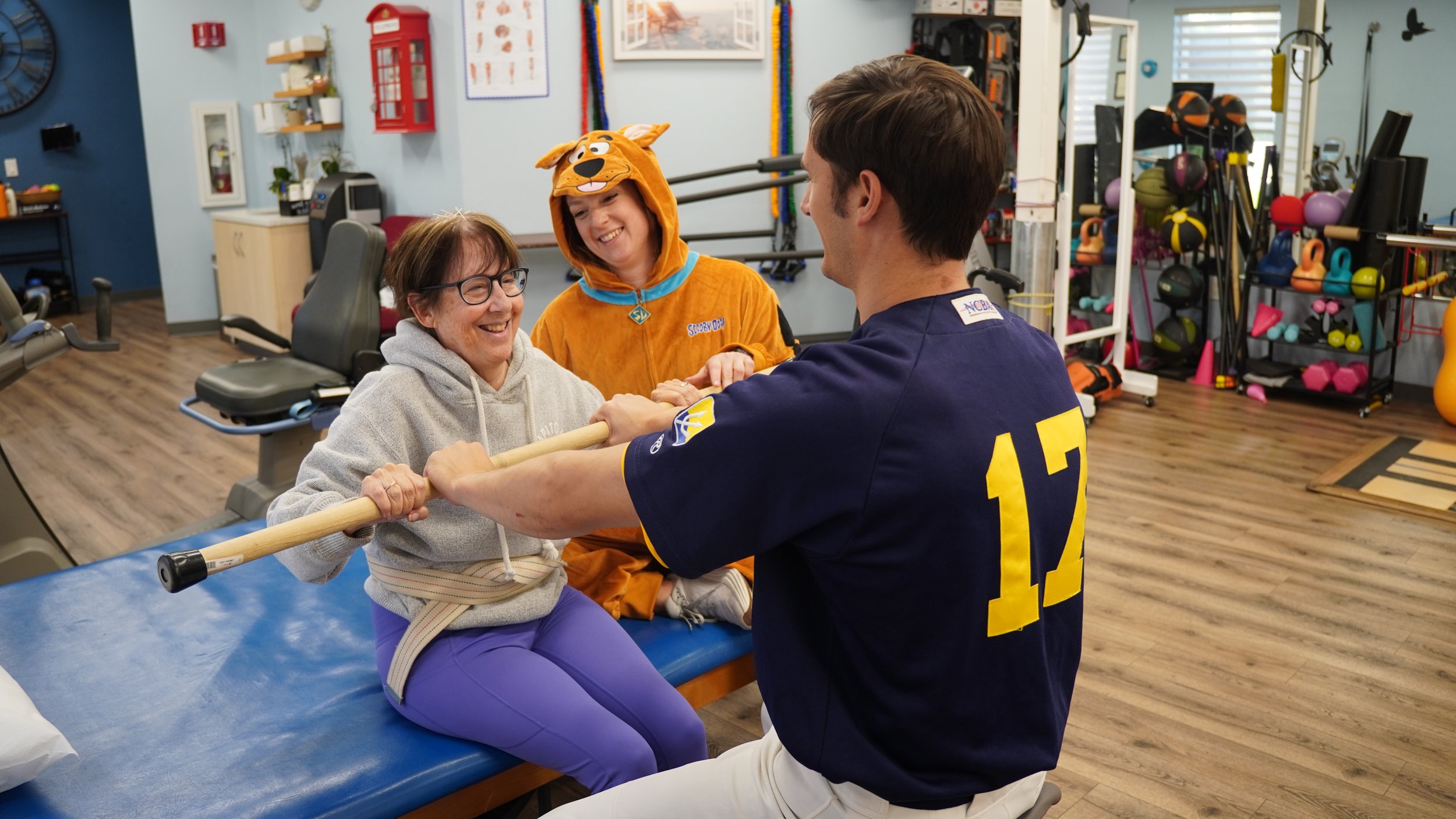 Patient laughing during seated physical therapy exercise with staff in Halloween costumes
