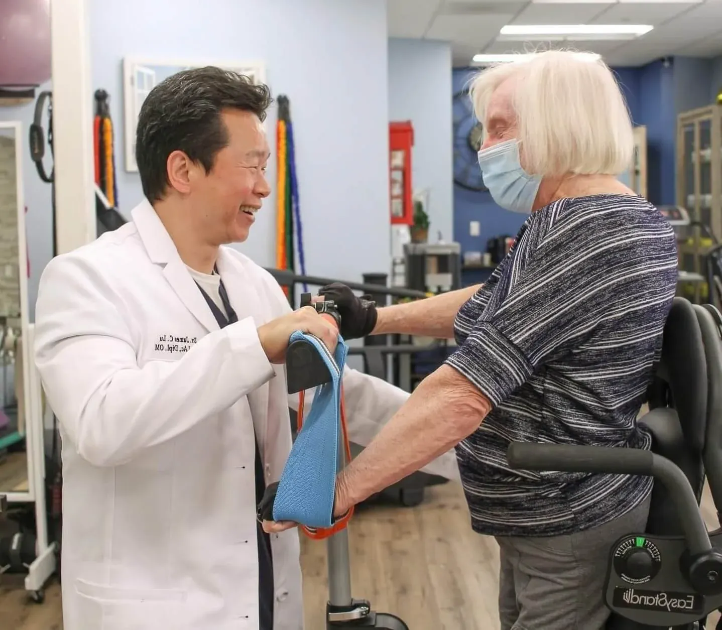 A healthcare professional and an elderly woman with a walker smiling at each other in a rehabilitation center.